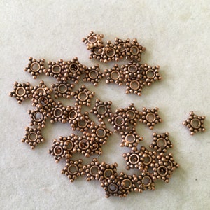 May include: A group of 20 copper-colored star-shaped bead spacers. Each spacer has a small hole in the center and is decorated with small raised dots.