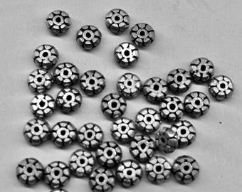 May include: A group of silver metal beads with a flower-like design. The beads are scattered on a white surface.
