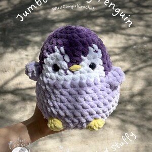 May include: A plush penguin toy made of chunky yarn in shades of dark purple, light purple, and white. It features black safety eyes, a small yellow beak, and yellow feet. The text "Jumbo Chonky Penguin @ArisCowgirlCrochet" and "Crocheted stuffy" is visible.
