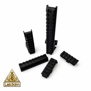 May include: Black Picatinny rails in various sizes and configurations are displayed against a white background. The rails are made of a matte black material and feature a series of horizontal grooves. The Lab3dm logo is in the lower left corner.