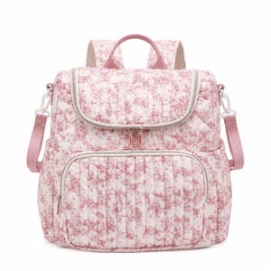 May include: A quilted backpack with a floral pattern in shades of pink and white. The bag has a top handle, adjustable shoulder straps, and multiple zippered compartments. The design includes a front pocket and a top flap with a zipper closure.