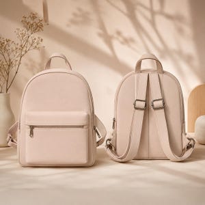 Pode incluir: Duas mochilas rosa claro. A mochila frontal tem um bolso frontal retangular com zíper. A outra mochila mostra as costas com alças ajustáveis e ferragens de metal. Ambas têm uma alça superior e um design curvo.