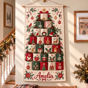 Könnte beinhalten: Ein hängender Adventskalender aus Stoff mit einem Weihnachtsbaum-Motiv und vierundzwanzig nummerierten Taschen. Das cremefarbene Textil zeigt festliche Illustrationen wie einen Kardinal, einen Lebkuchenmann und ein Rentier. Der Name Amelia ist unten in roter Schrift aufgedruckt.