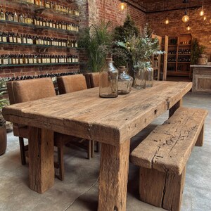 Peut inclure: Une table &agrave; manger rustique en bois avec un banc et des chaises assortis. La table est en bois de r&eacute;cup&eacute;ration et a une finition naturelle. Des bouteilles en verre transparent avec des bouchons en li&egrave;ge sont sur la table.