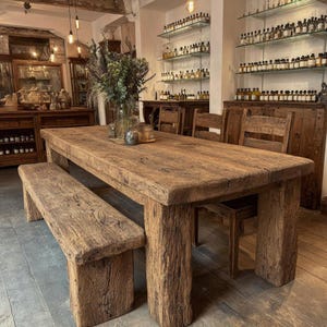 Peut inclure: Une table &agrave; manger rectangulaire en bois rustique avec un banc assorti. La table et le banc sont en bois vieilli, mettant en valeur le grain et la texture naturels. La table est soutenue par des pieds &eacute;pais et carr&eacute;s. La pi&egrave;ce a une esth&eacute;tique vintage.