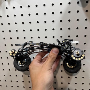 May include: A black and gold speckled remote control car chassis featuring a complex suspension system, four black rubber tires with gold-accented wheel hubs, and a metallic frame structure designed for high-performance off-road model racing.