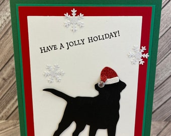 May include: A Christmas card with a black dog silhouette wearing a Santa hat. The card has a white background with the text "Have a Jolly Holiday!" and decorative snowflakes. The card is layered with red and green borders.