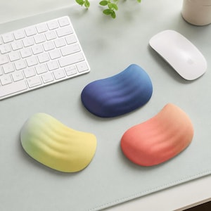 May include: Three ergonomic wrist rests with a smooth, curved, bean-like shape. One rest is a gradient of yellow to light green, one is a solid deep blue, and one is a gradient of orange to light pink. Each rest has a soft, matte texture.