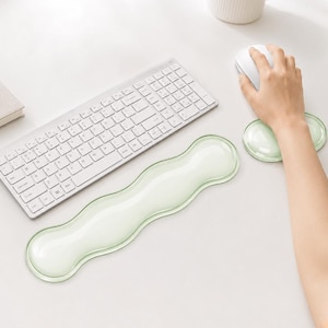 May include: A light green, translucent, wavy-shaped keyboard wrist rest and a matching oval mouse wrist rest. The keyboard rest is elongated with a curved design, while the mouse rest is smaller and rounded, both featuring a smooth surface.