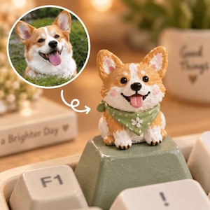 Op de afbeelding: Een klein, handbeschilderd harsfiguurtje van een Corgi-hond met een tan en witte vacht, met een saliegroene bandana met een wit bloemenpatroon. Het figuurtje is gemonteerd op een saliegroene mechanische toetsenbordtoets tussen witte toetsen.