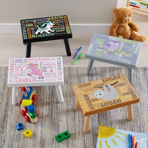 May include: Four rectangular wooden step stools with four legs each. Each stool features a unique animal graphic and a repeating name pattern: a black stool with a dog named Mason, a white stool with a unicorn named Amelia, a grey stool with an owl named Kinsley, and a tan stool with a sloth named Logan.