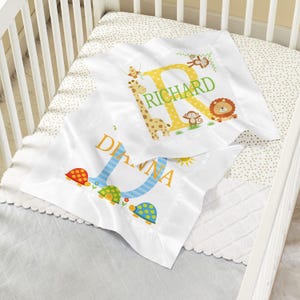 May include: Two white square pillowcases with satin borders. One features a yellow letter R, the name RICHARD, a giraffe, monkeys, and a lion. The other features a blue striped letter D, the name DIANNA, and three colorful patterned turtles.