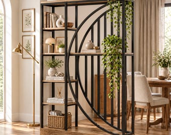 May include: A tall room divider shelf featuring a black metal frame with a large circular design and light wood shelves. The unit holds various decorative items including books, small potted plants, a lamp, and a woven basket at the base.