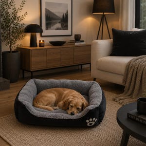 以下が含まれることがあります： ゴールデンレトリバーが寝ている黒とグレーの犬用ベッド。ベッドは、柔らかい内側と白い足跡が付いています。犬はベッドの中に丸まっており、リビングルームのニュートラルカラーのラグの上に置かれています。