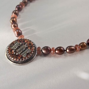 May include: A brown pearl and sunstone necklace with a silver and copper pendant featuring a geometric design.