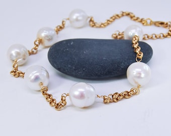 May include: A gold chain necklace with white pearls. The necklace is on a gray stone surface.