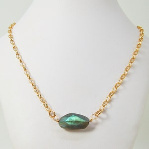 May include: A gold chain necklace with a single, large, green gemstone pendant.