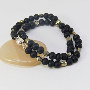 Puede incluir: Un brazalete de cuentas negras y doradas con cierre magnético. El brazalete está hecho con cuentas de ónix negro y pirita.