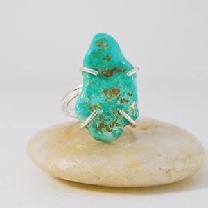 May include: A turquoise ring with a silver setting. The turquoise is a natural stone with a unique shape and a green and brown colour.