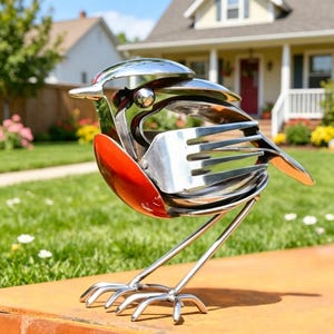 May include: A whimsical metal bird sculpture crafted from repurposed silverware. The bird features a red breast, a silver body, and is perched on delicate metal legs. This unique piece adds a touch of artistic flair to any garden or home decor.