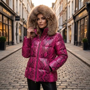 Puede incluir: Una chaqueta acolchada de color rosa brillante con un estampado de piel de serpiente en negro, cuello alto y una capucha grande con borde de piel sintética marrón. La prenda cuenta con cierre de cremallera frontal y mangas largas.