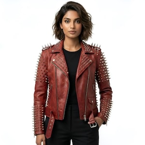 Könnte beinhalten: Rote Lederjacke mit silbernen Stacheln auf den Schultern und Ärmeln. Die Jacke hat einen Reißverschluss, einen Gürtel in der Taille und ein schwarzes Futter. Das Model trägt ein schwarzes Oberteil und eine schwarze Hose.