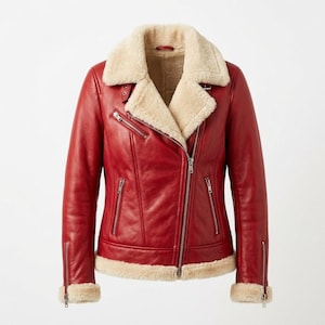 Puede incluir: Una chaqueta de cuero rojo vibrante con un cuello ancho de borreguillo color crema y ribetes a juego en el dobladillo y los puños. La chaqueta incluye un cierre de cremallera frontal asimétrico, dos bolsillos verticales con cremallera y cremalleras en las muñecas.