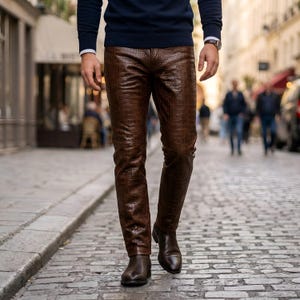 Puede incluir: Pantalones marrones con un patrón de textura de piel de cocodrilo. Los pantalones se combinan con un suéter azul oscuro de manga larga y botas de cuero marrón oscuro. La prenda tiene un corte recto y una cintura clásica con cierre de botón.