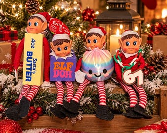 May include: Four elf dolls with red and white striped legs and black shoes. One holds a yellow box labeled .4oz Santa's BUTTER, one a purple box labeled ELF DOH, one a pastel iridescent sphere, and one a green chain with the number 67.