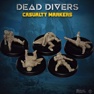 Puede incluir: Cinco figuras en miniatura de color tostado etiquetadas como Dead Divers Casualty Markers, cada una en una pose diferente de caída o reposo sobre una base negra circular. Las figuras llevan equipo táctico y cascos, algunas con capas. Texto: 32mm stl presupported.