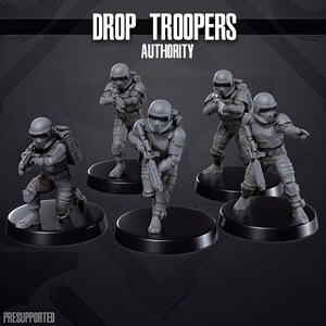 Könnte beinhalten: Eine Sammlung grauer Drop Troopers-Miniaturen, jede mit einer Waffe. Die Figuren stehen auf schwarzen, kreisförmigen Sockeln. Der Text "DROP TROOPERS AUTHORITY" steht oben und "PRESUPPORTED" unten.