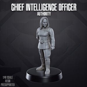 Może przedstawiać: Szara miniaturowa figurka z żywicy przedstawiająca Chief Intelligence Officer Authority na okrągłej podstawie. Postać ma włosy do ramion, tunikę z wysokim kołnierzem i odznaką na piersi, pasek z klamrą oraz wysokie buty. Skala 1:48.