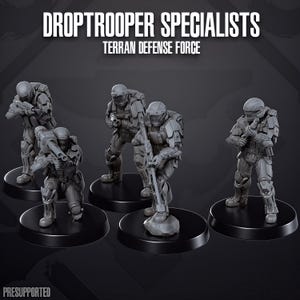 Könnte beinhalten: Fünf graue Miniatur-Soldatenfiguren mit der Aufschrift DROPTROOPER SPECIALISTS TERRAN DEFENSE FORCE. Jede Figur trägt taktische Rüstung, Helme und verschiedene Waffen, darunter Gewehre und einen schweren Werfer, auf runden schwarzen Sockeln.