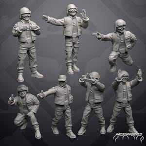 Op de afbeelding: Een set van zeven grijze miniatuurfiguurtjes die soldaten in tactische uitrusting met helmen, brillen en utility-jacks voorstellen. De figuren staan in verschillende houdingen, sommige staand en sommige gehurkt, met gebarende handen.