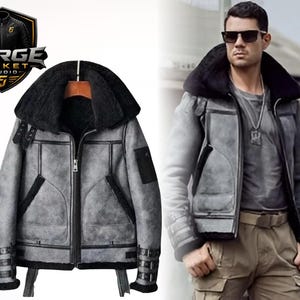 Puede incluir: Chaqueta de borrego gris con cuello de piel negra y ribetes negros. La chaqueta tiene cierre de cremallera, bolsillos y detalles de hebillas en las mangas. El logotipo "FORGE JACKET STUDIO" es visible.