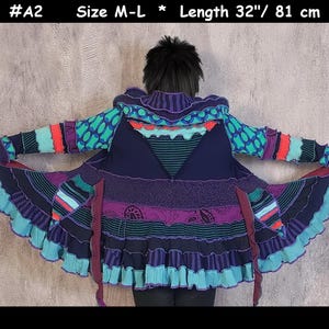 May include: A multi-coloured patchwork coat featuring a hood, long sleeves, and a flared hem with ruffled edges. The garment displays various patterns in shades of purple, teal, and blue, with a length of 81 cm and size M-L label #A2.