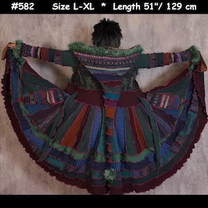 May include: A multi-coloured, long, knitted cardigan with a hood. The cardigan is made of different coloured stripes and has a layered, ruffled hem. The cardigan is size L-XL and 129 cm long.