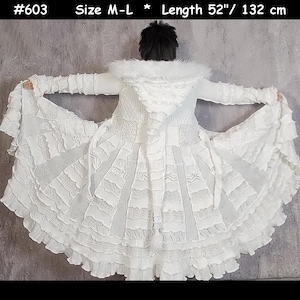 May include: A white hooded coat featuring a patchwork design of various knit textures, ruffled fabric panels, and a faux fur trim around the hood. The garment is labelled #603, size M-L, and measures 132 cm in length with long sleeves and a flared hem.