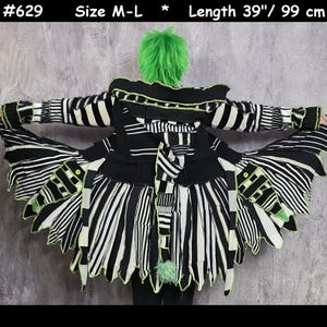 Peut inclure: Un manteau à rayures noires et blanches avec un ourlet déchiqueté et superposé, agrémenté de bordures vert néon. Le vêtement possède une capuche, des manches longues et une queue. Le texte indique #629, taille M-L, longueur 99 cm.