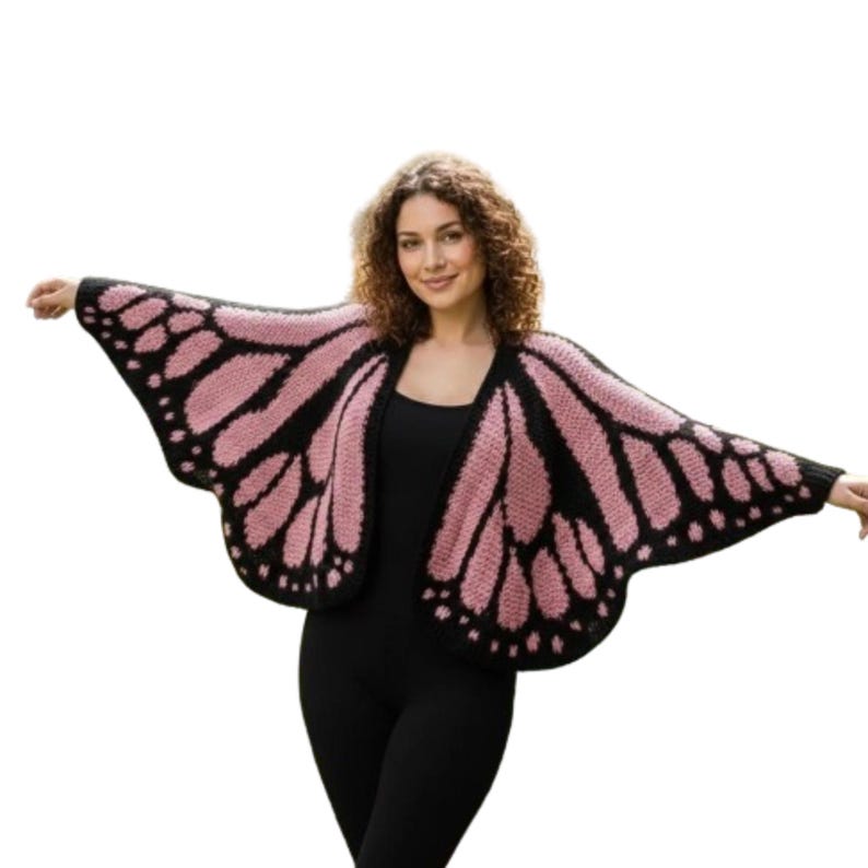 May include: A knitted butterfly wing wrap in black and pink. The wrap is open in the front and has a wing-like design with black outlines and pink filling. The person in the image is wearing a black outfit.