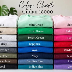 Może przedstawiać: Wzornik kolor&oacute;w bluz Gildan 18000 przedstawiający trzy pionowe stosy złożonej odzieży w r&oacute;żnych kolorach. Tekst brzmi Color Chart Gildan 18000, a po nim następują etykiety dla każdego koloru, w tym biały, piaskowy, popielaty, szary, zielony, niebieski, r&oacute;żowy, czerwony i fioletowy.