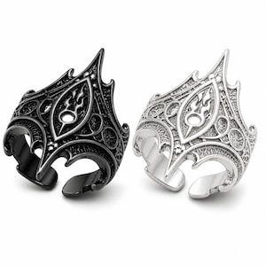 May include: Two ornate rings, one black and one silver, are displayed. Each ring features a detailed, symmetrical design with a central flame motif and open adjustable bands. The rings have a gothic or fantasy aesthetic.