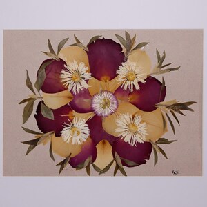 May include: A framed floral arrangement featuring a circular design of pressed flowers. The arrangement includes deep purple petals, yellow petals, white daisies, and green leaves, all set against a beige background.