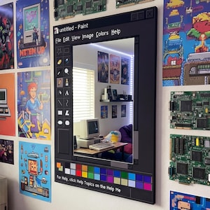 May include: A black framed mirror designed to look like the Windows Paint application. The mirror reflects a room with a computer setup and posters. The text "untitled - Paint" is visible at the top, with the colour palette at the bottom.