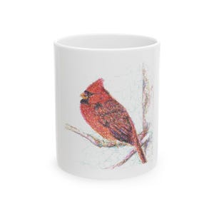 May include: White ceramic mug featuring a detailed illustration of a red cardinal bird perched on a branch. The bird is rendered in shades of red, brown, and black, with a textured, pen-like style. The mug is cylindrical and has a glossy finish.