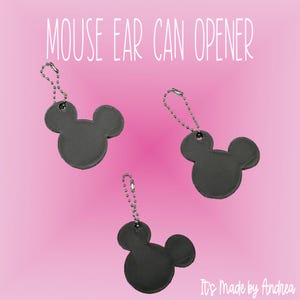 May include: Three dark gray mouse ear can openers with silver ball chains. The text MOUSE EAR CAN OPENER is at the top and It's Made by Andrea is at the bottom. Each opener features a circular head with two smaller circular ears attached.