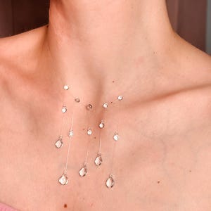 May include: A clear nylon thread necklace featuring multiple dangling clear crystal beads in various sizes. The beads are arranged in a cascading pattern, with some shaped like small spheres and others like teardrops, suspended at different lengths.