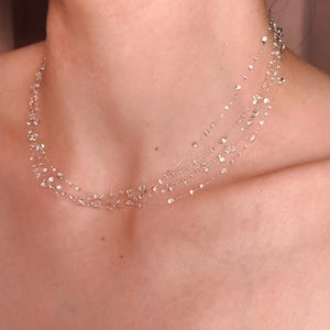 May include: A multi-strand silver-toned necklace featuring delicate, thin chains adorned with numerous small, clear, reflective circular accents spaced along the length of each strand, creating a layered, shimmering effect around the neck.