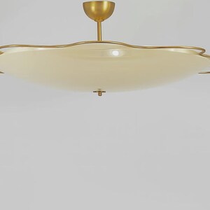 May include: A ceiling light fixture featuring a wide, shallow, cream-colored disc shade with a scalloped edge. The shade is framed by a thin, gold-toned metal wire that follows the wavy perimeter. A central gold-toned rod connects to a canopy.