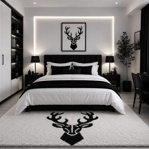 Puede incluir: Un dormitorio con una paleta de colores en blanco y negro, que incluye una cama entre dos mesitas de noche, una alfombra blanca con un gráfico de cabeza de ciervo negro, arte de pared a juego, armarios blancos y un escritorio negro.